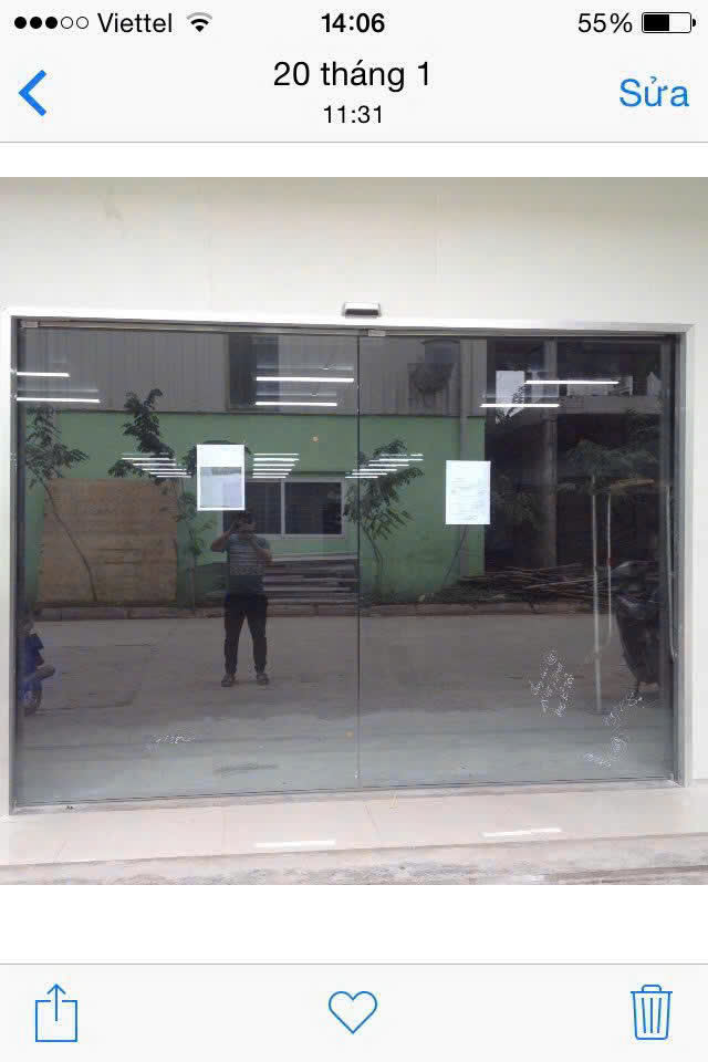Cửa kính cường lực mặt tiền rộng với khung nhôm, phản chiếu người chụp và cảnh bên ngoài
